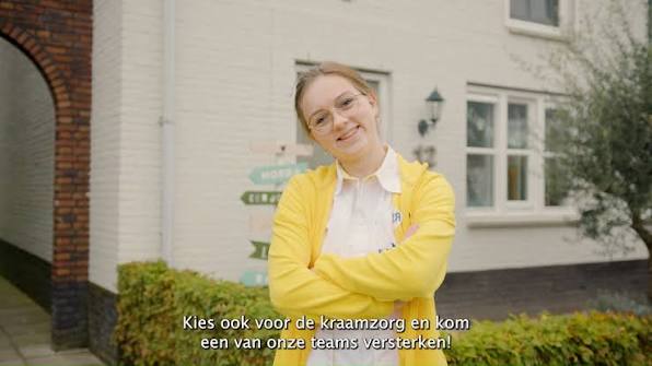 Vriendelijke vrouw in een gele jas staat buiten met armen over elkaar en glimlacht; ondertiteling over kraamzorg en het team versterken.
